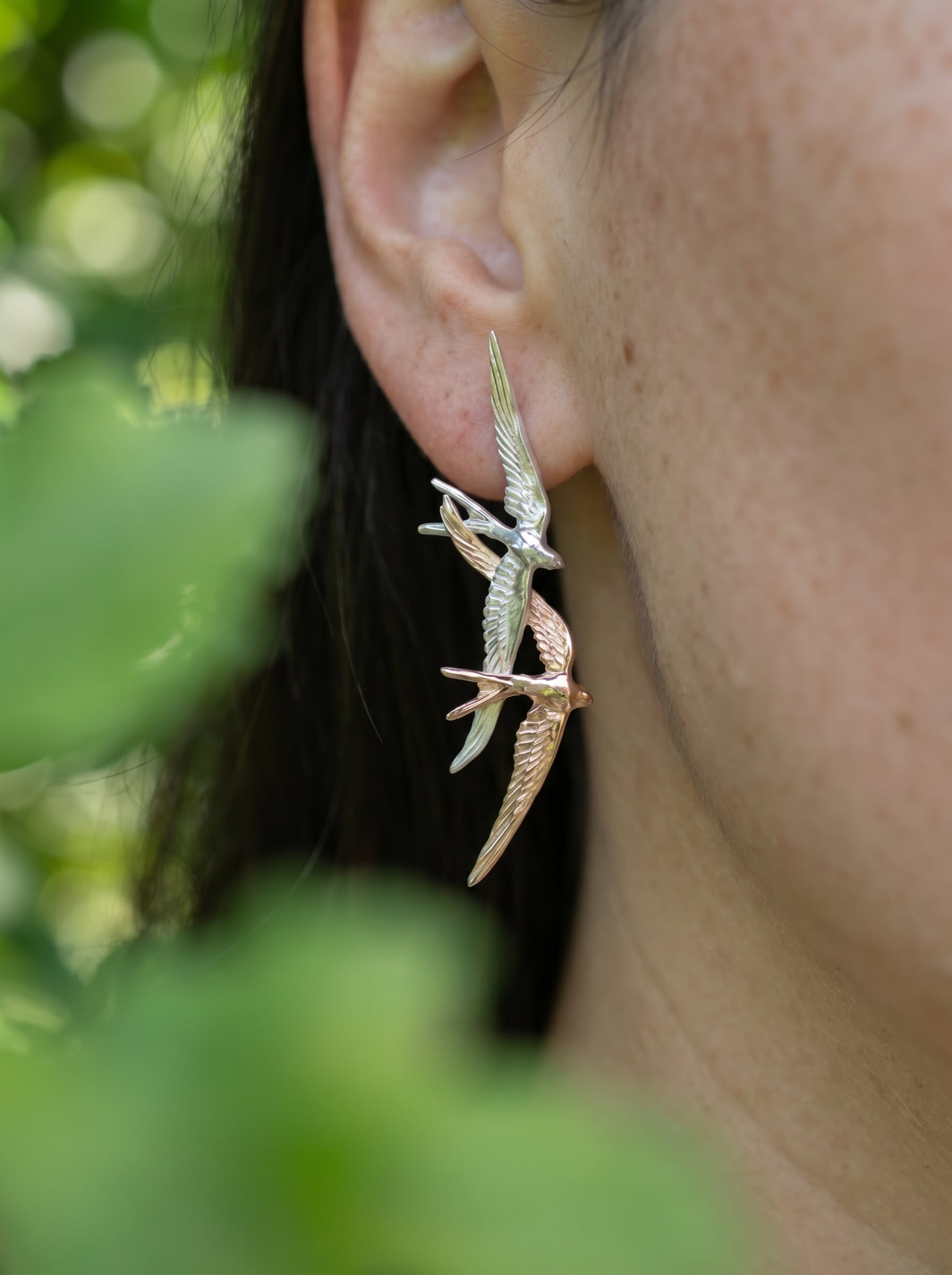 Swallow Flight Stud Earrings worn on ear, showing asymmetrical design and soft metallic reflections against natural light.