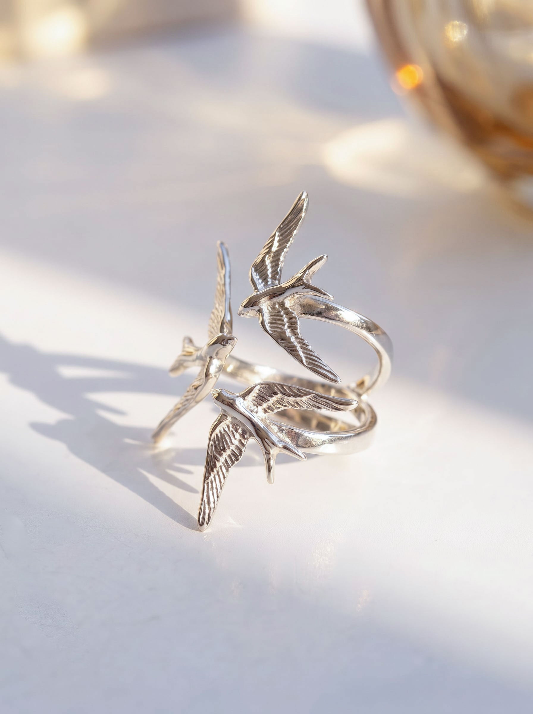 Gold and silver Swallow Gathering Rings side by side, capturing the mirrored bird forms and polished surfaces.
