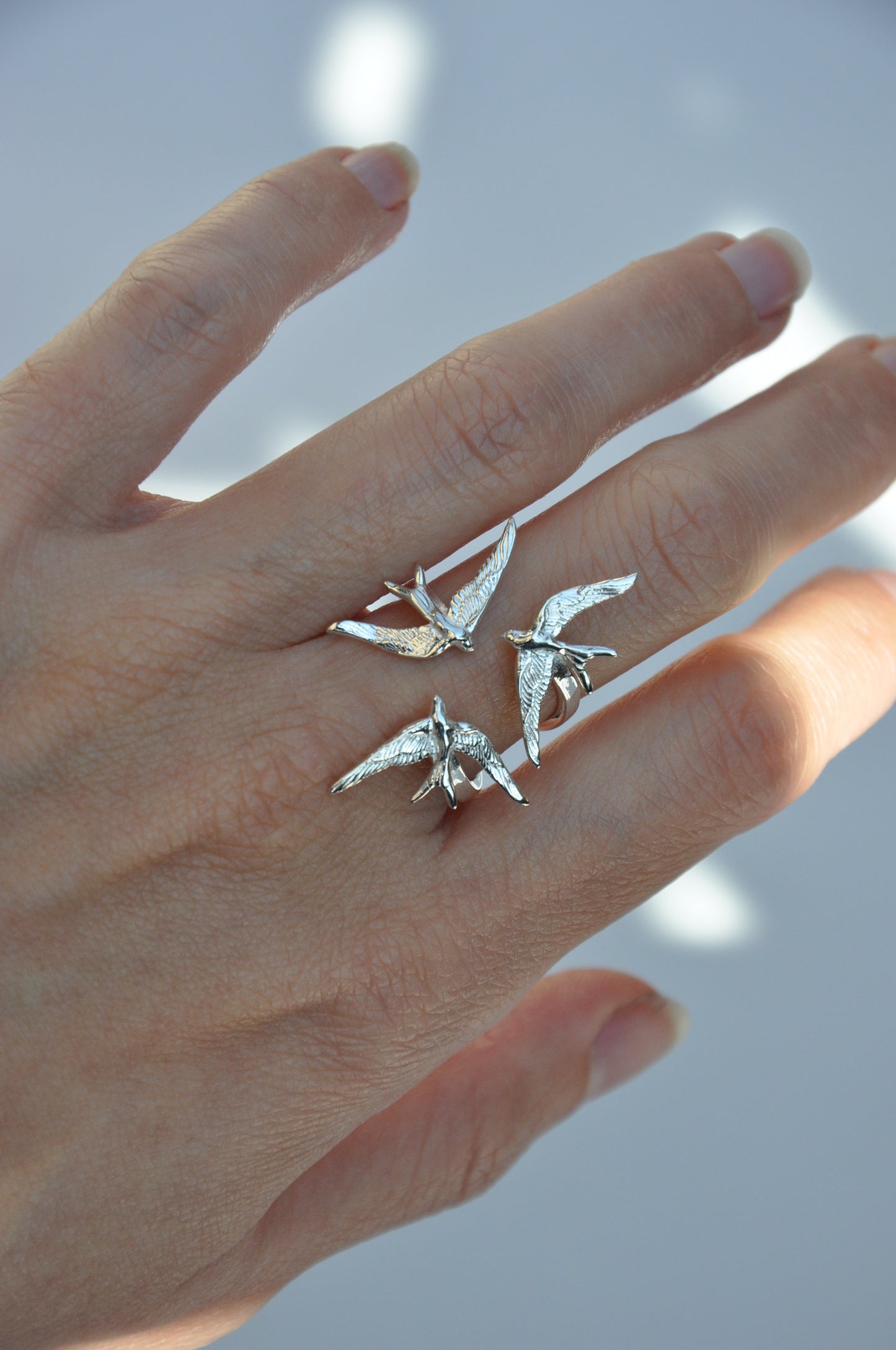 Swallow Gathering Ring worn on hand under natural light, showing the three birds meeting in a moment of harmony.