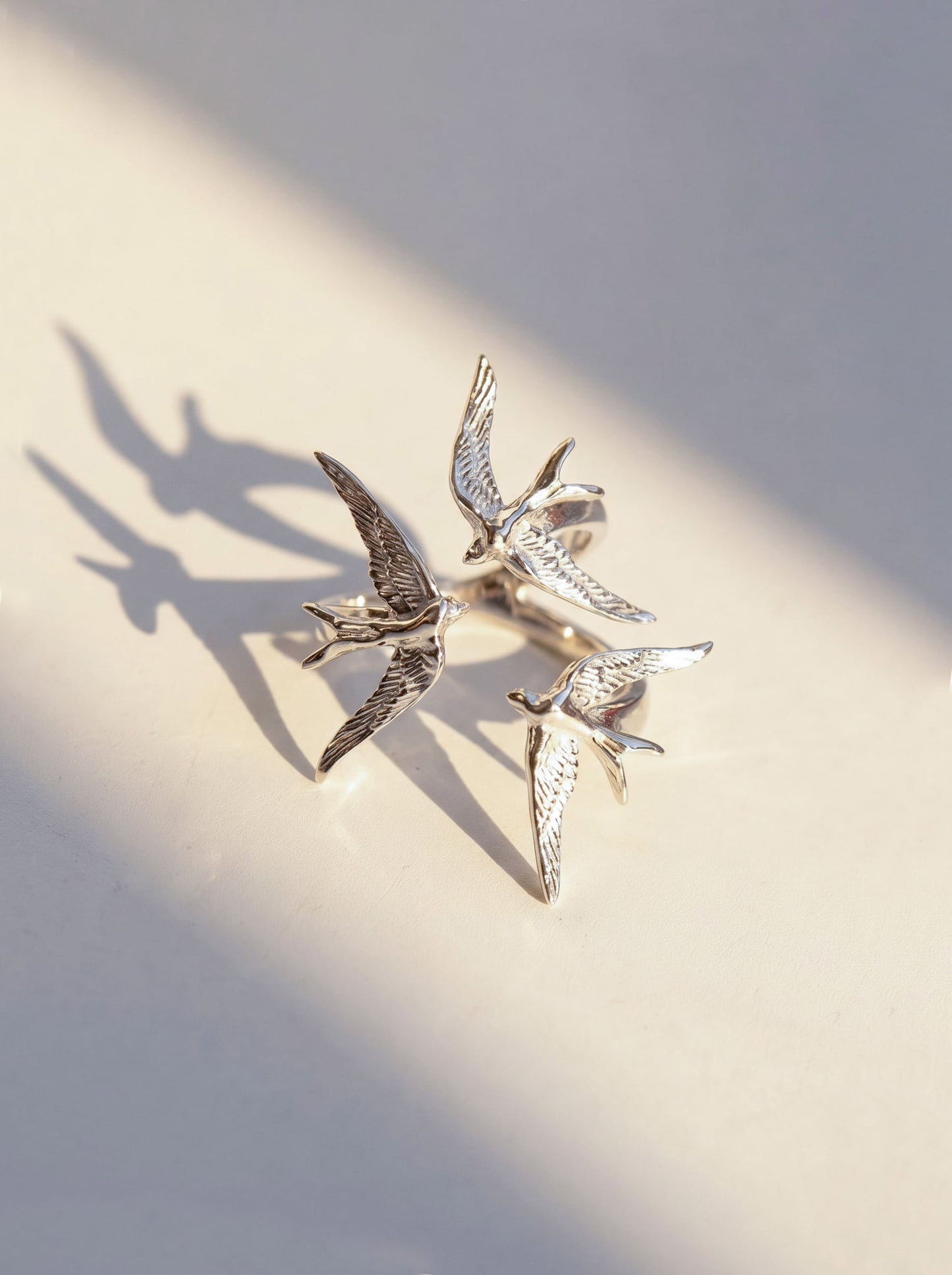 Silver Swallow Gathering Ring photographed flat, showing detailed feather engraving and circular alignment of the birds.
