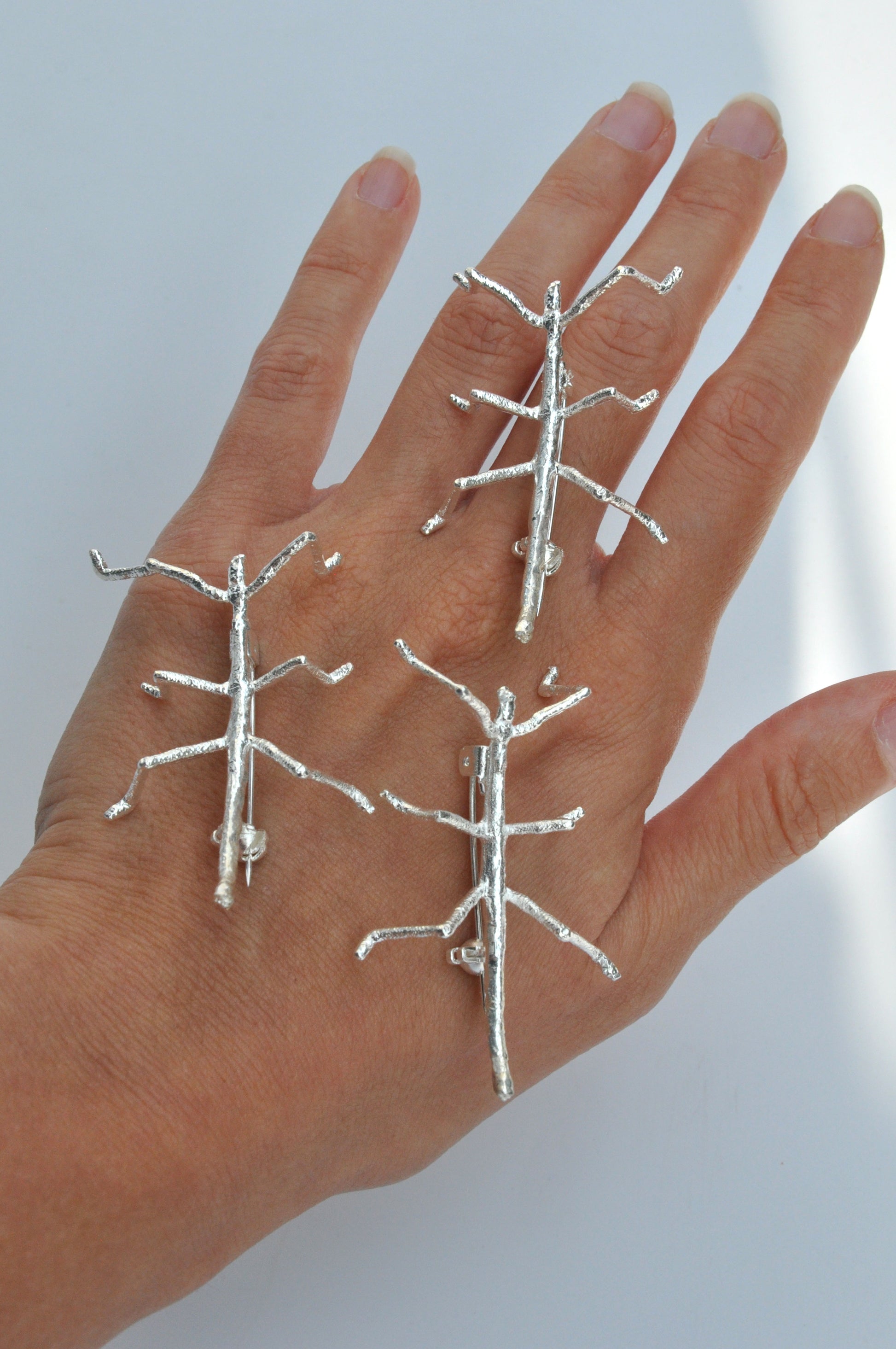 Top view of three silver stick insect brooches displayed on a hand, highlighting their delicate and detailed design.
