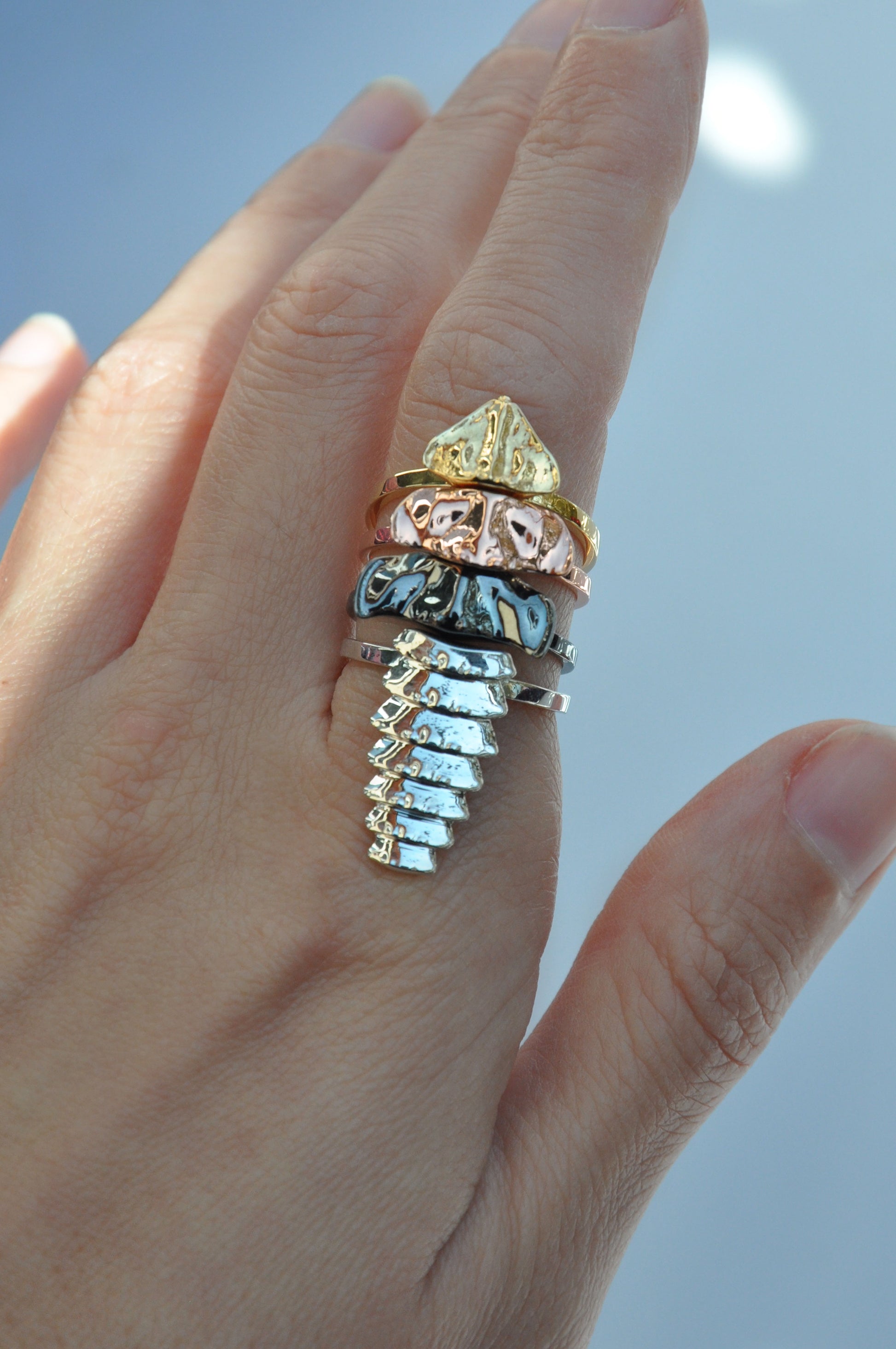 Hand wearing a mixed‑metal trilobite beetle stacking ring set with silver, gold, rose gold, and black rhodium segments forming a sculptural, elongated silhouette.