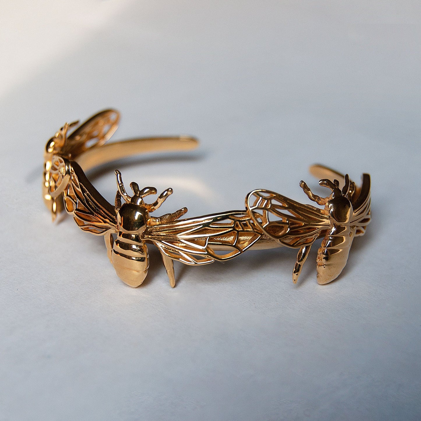 Gold bee bracelet cuff displayed on white background, highlighting cut-out wing details.