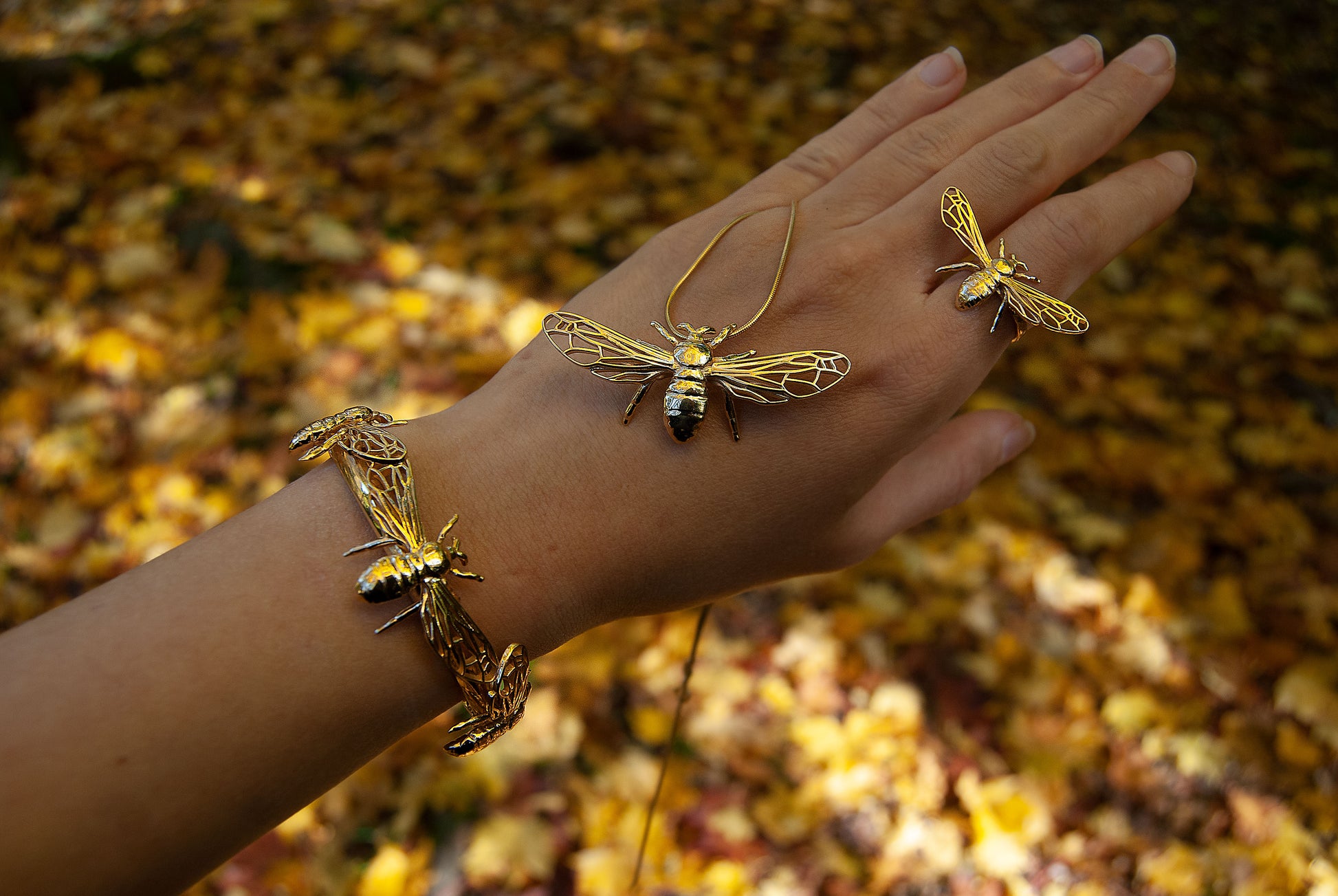 Gold bee charm cuff bracelet catching sunlight in natural setting.