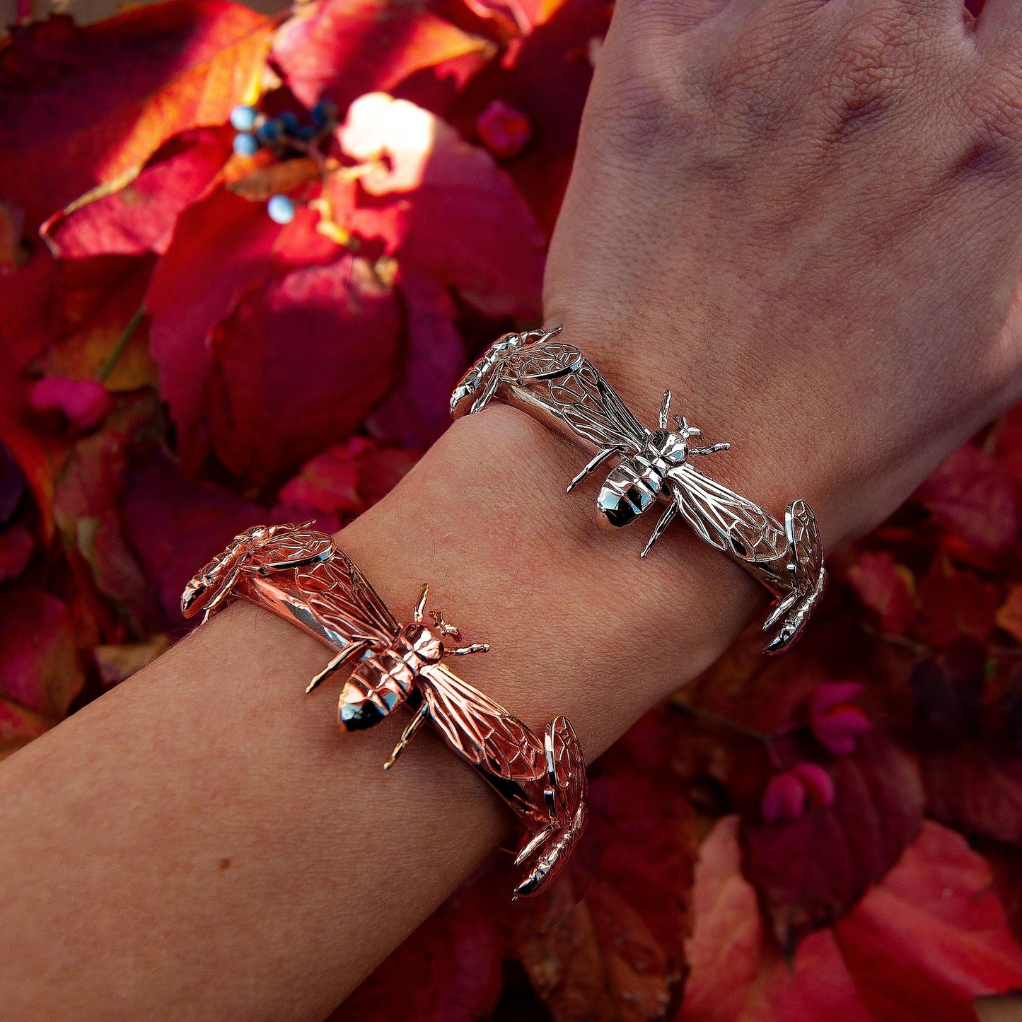 Silver and rose gold bee cuff bracelets stacked on wrist for mixed metal style.