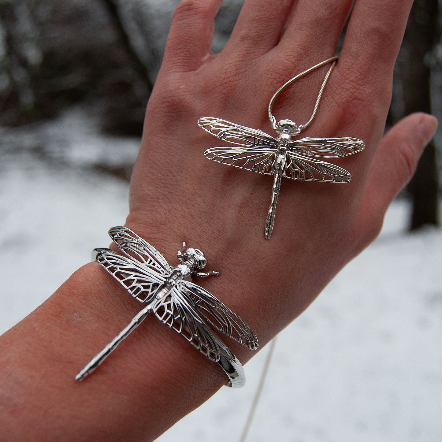 Silver Dragonfly Pendant and Bracelet worn together on hand, styled in outdoor setting with soft shadows.