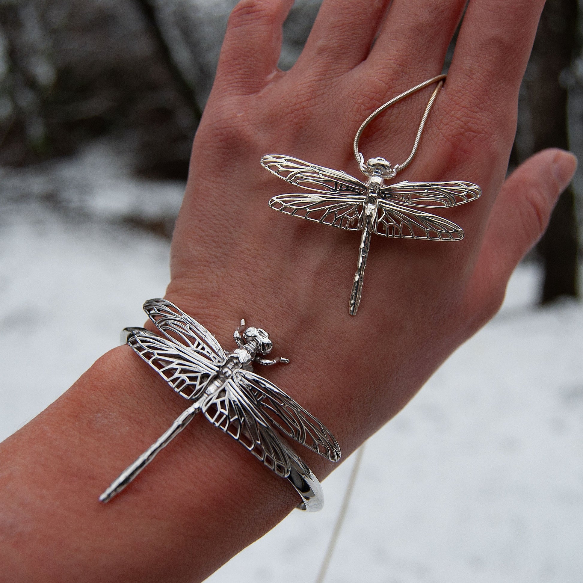 Silver Dragonfly Pendant and Bracelet worn together on hand, styled in outdoor setting with soft shadows.
