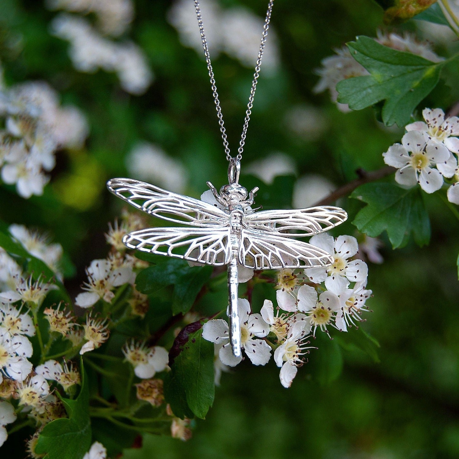 Handcrafted dragonfly pendant resting on a leaf, nature-inspired silver charm jewelry.