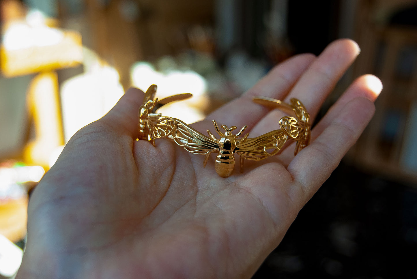 Close-up of hand holding gold bee bracelet at a slight angle, highlighting wing texture.