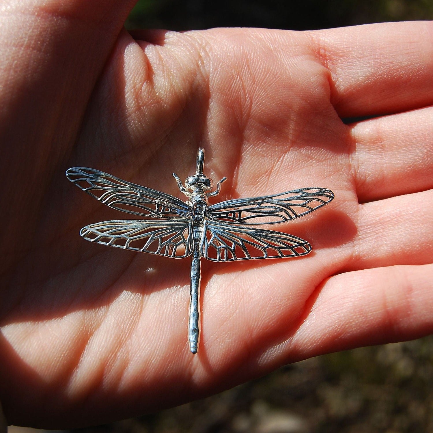 Hand holding symbolic dragonfly pendant at an angle, handmade sterling silver charm