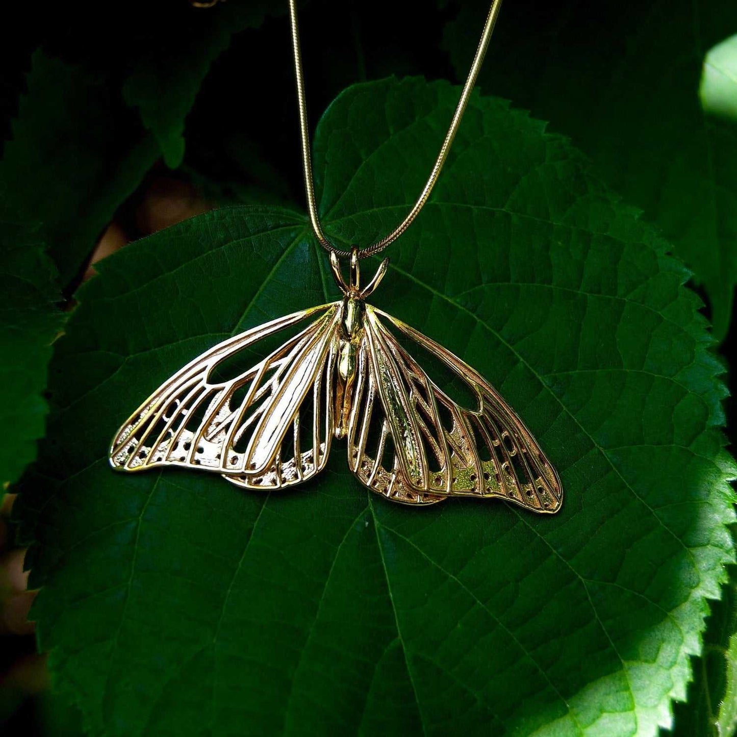 Gold Monarch Butterfly pendant resting on a green leaf, capturing natural contrast and shine.