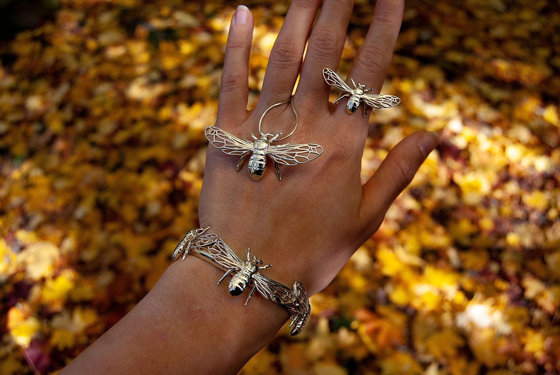 Close-up of nature-inspired bee bracelet in silver nestled among wild greenery.