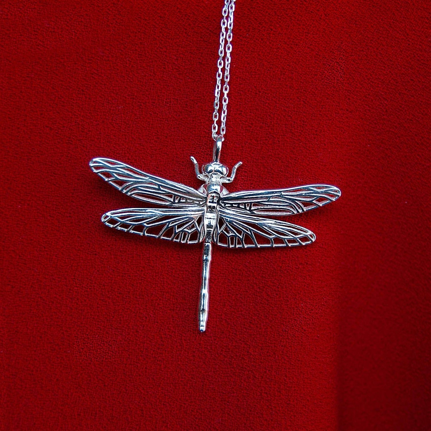 Sterling silver dragonfly pendant displayed on a rich red surface, artistic necklace detail